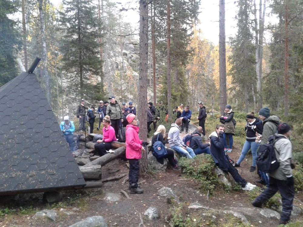Paljon ihmisiä metsässä laavun läheisyydessä.