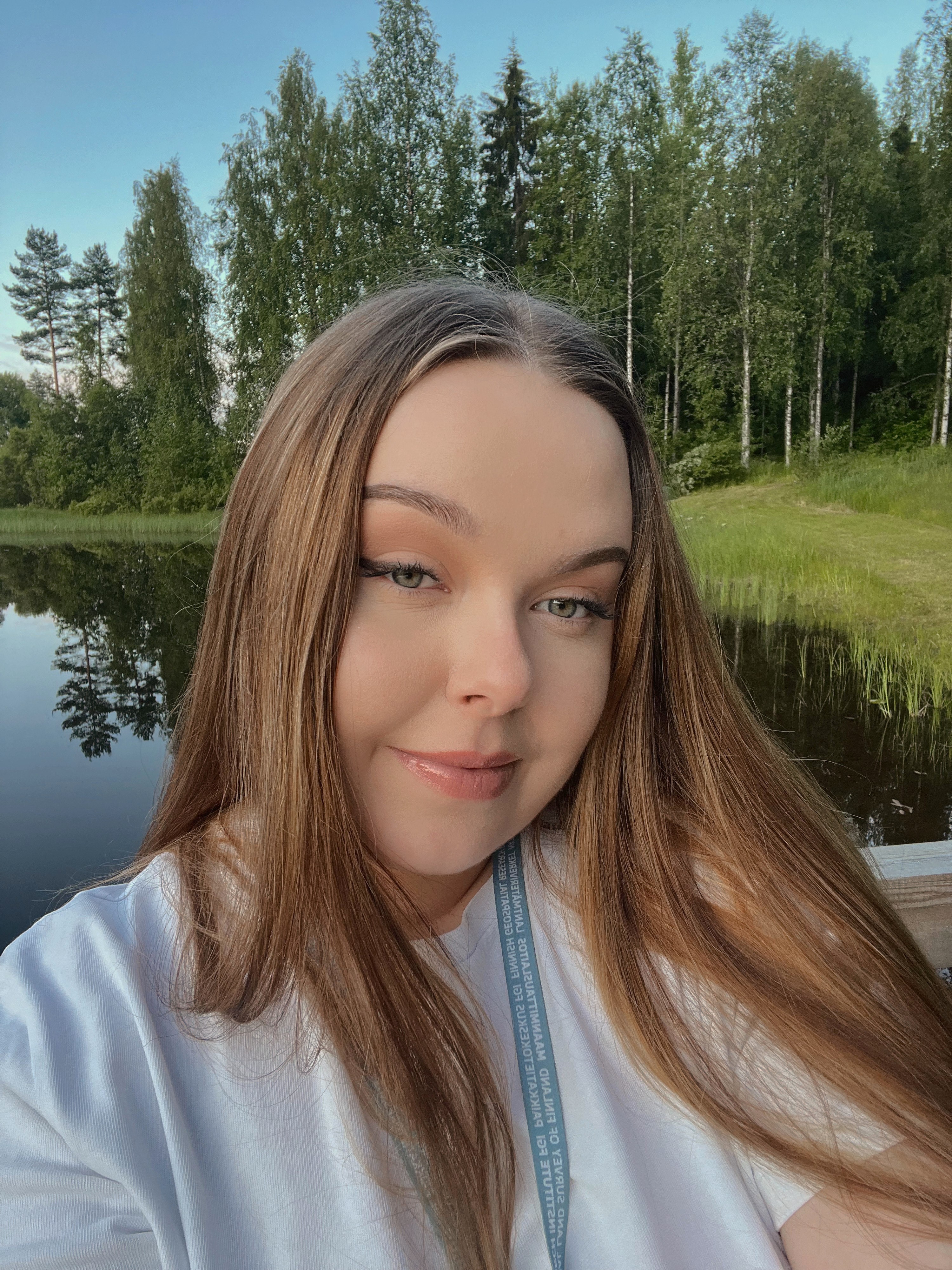 Nuori nainen katsoo kameraan hymyillen. Taustalla järvi ja puita.