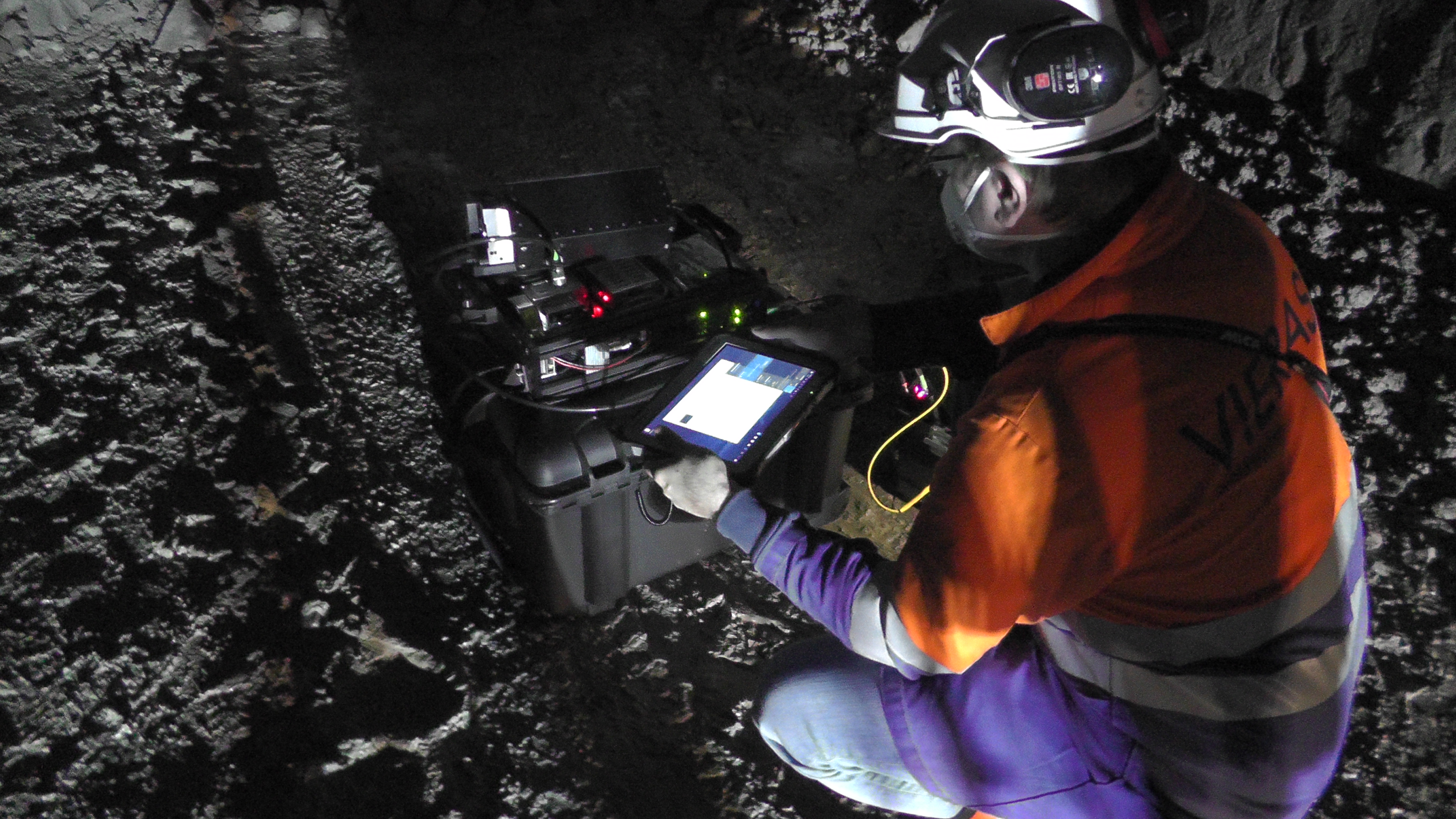 Kuvassa työntekijä mittaa malmipitoisuuksia pimeässä kaivoksessa.