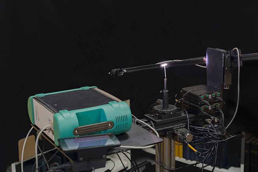 Kuvassa FGI:n avaruusgoniospektrometrilaitteistoa. Kirkas piste keskellä on näyte.  Varren päässä oleva linssi kerää valon kuituun ja vie sen etualla näkyvään vihreään spektrometriin.