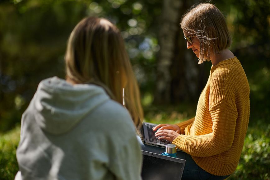 Två personer sitter i en park och skriver på en dator