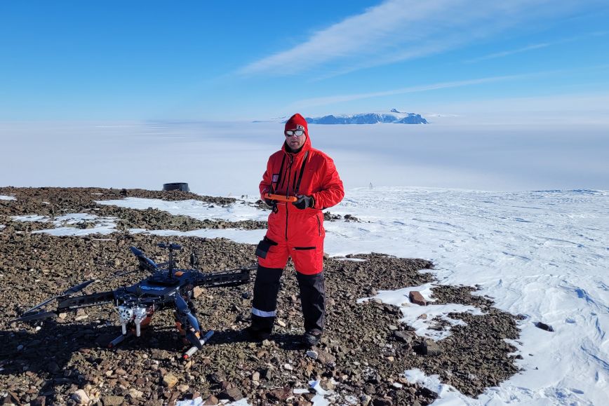 In a sunny and snowy landscape, the researcher stands in front of a large drone.