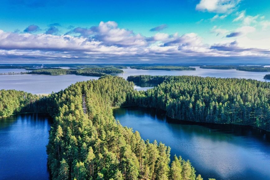 Ilmakuva järvimaisemasta, jossa sinistä vettä ja vihreiden metsien peitossa olevia saaria. Horisontissa pilviä.