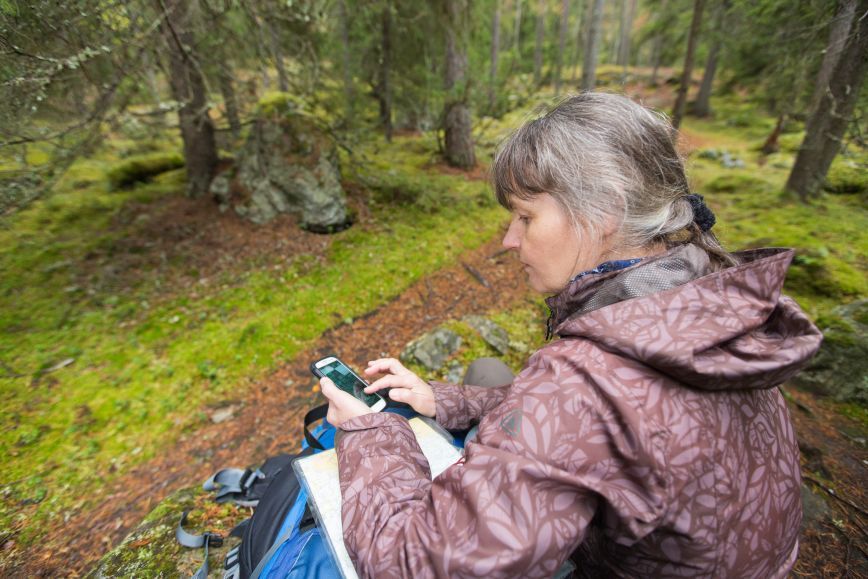 Nainen on istahtanut metsässä kivelle katsomaan karttaa.