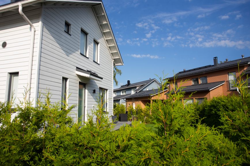 Vitt egnahemshus med grön växtlighet framför och ett orange hus i bakgrunden.