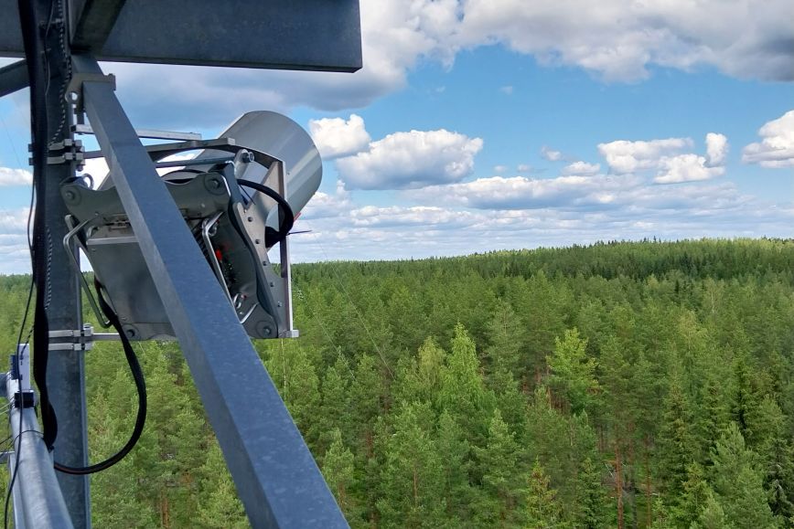 Pieni laserkeilain kiinnitettynä torniin metsän reunassa