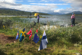 Kolmen valtakunnan rajapyykki Kilpisjärvellä. Lapset katselevat keltaista rajapyykkiä. Maassa Pohjoismaiden liput.