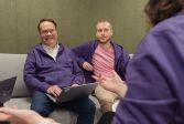 Antti and Joonas are sitting on the sofa wearing purple hoodies.