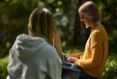 Två personer sitter i en park och skriver på en dator