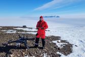 In a sunny and snowy landscape, the researcher stands in front of a large drone.