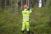 Lantmäteriingenjören står med ryggen mot kameran i gula skyddskläder och tittar på skärmen på sin enhet för att fastställa gränsen i skogen.