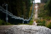 The barrier fence consists of a metal mesh fence, an adjacent road, a treeless area and a technical monitoring system.