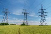 Kraftledningar löper på höga stolpar över en åker