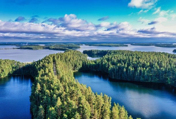 Aerial view of a lake landscape with blue water and islands covered in green forests. Clouds on the horizon.