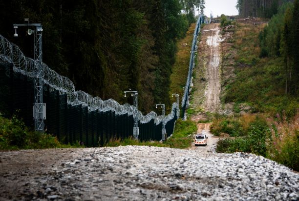På bilden syns ett metallnätstängsel, en väg som löper intill detta och ett tekniskt övervakningssystem