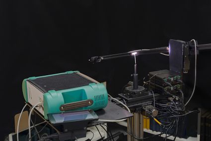 FGI’s space goniospectrometer equipment pictured. The bright dot in the centre is a sample.  The lens at the end of the rod collects the light in a fibre and takes it to the green spectrometer shown at the front.