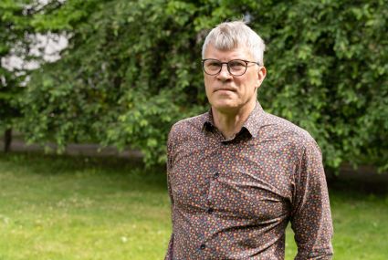 Jukka Rahkonen, en korthårig person med glasögon står ute i en grönskande miljö.