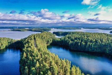 Flygfoto över ett sjölandskap med blått vatten och öar täckta av gröna skogar. Moln vid horisonten.