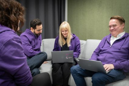 Neljä ihmistä istuu sohvalla, kahdella on kannettava tietokone. Kaikilla ihmisillä on päällään violetit hupparit.