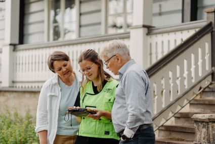 Pariskunta keskustelee maanmittausinsinöörin kanssa talonsa pihalla.