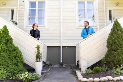 Vaalea puurivitalo ja sen edessä kaksi asukasta omilla portaillaan seisomaassa