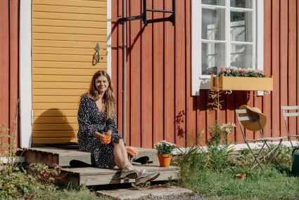 A woman is spending time outside her cottage in a summer landscape.